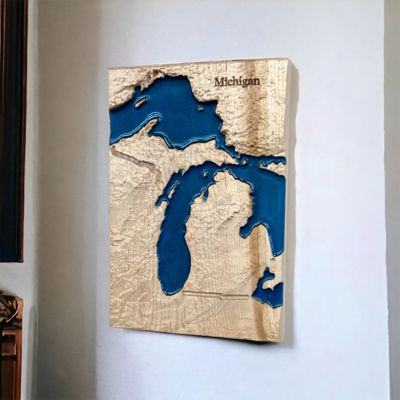 Wooden wall art of a topographic map of Michigan with blue water features on a white wall.