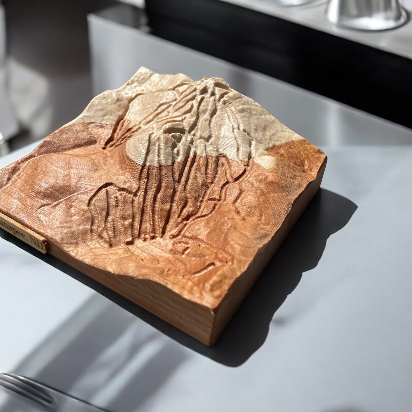 A wood-carved 3D relief map of Sunapee ski mountain, featuring details of the terrain, placed on a flat surface.
