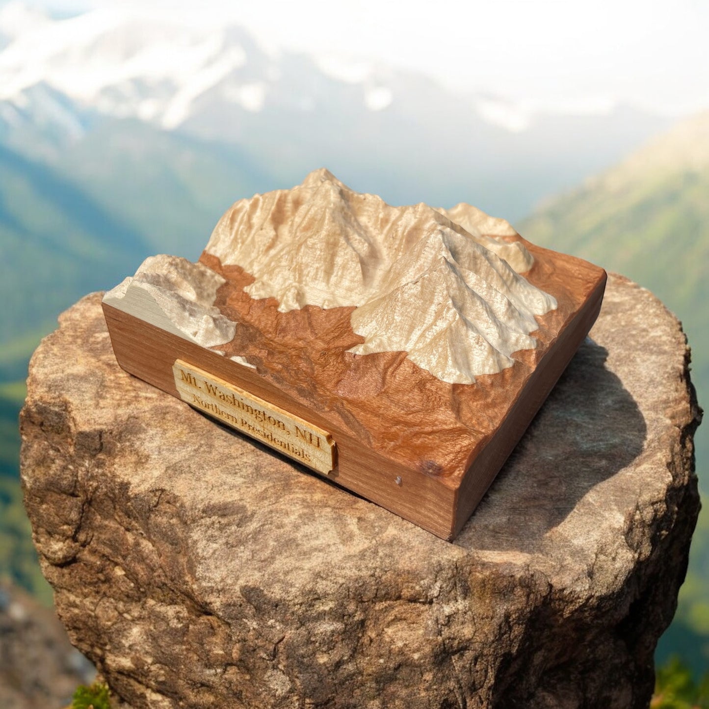 A wooden 3D relief map of Mt Washington, placed on a rock with a scenic landscape in the background.