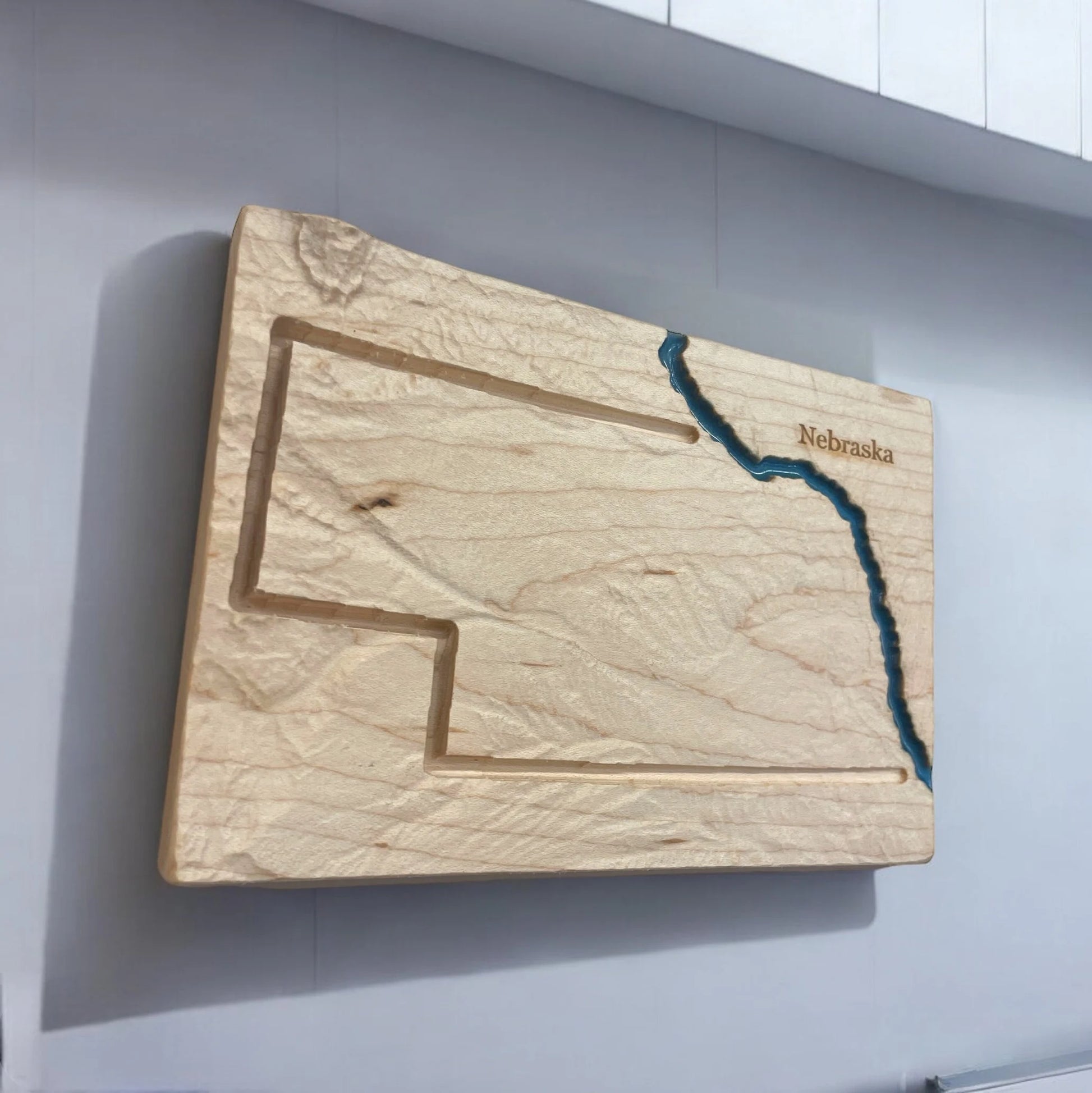Wooden topo map with engraved outline of Nebraska on a white wall with Missouri rive in blue epoxy