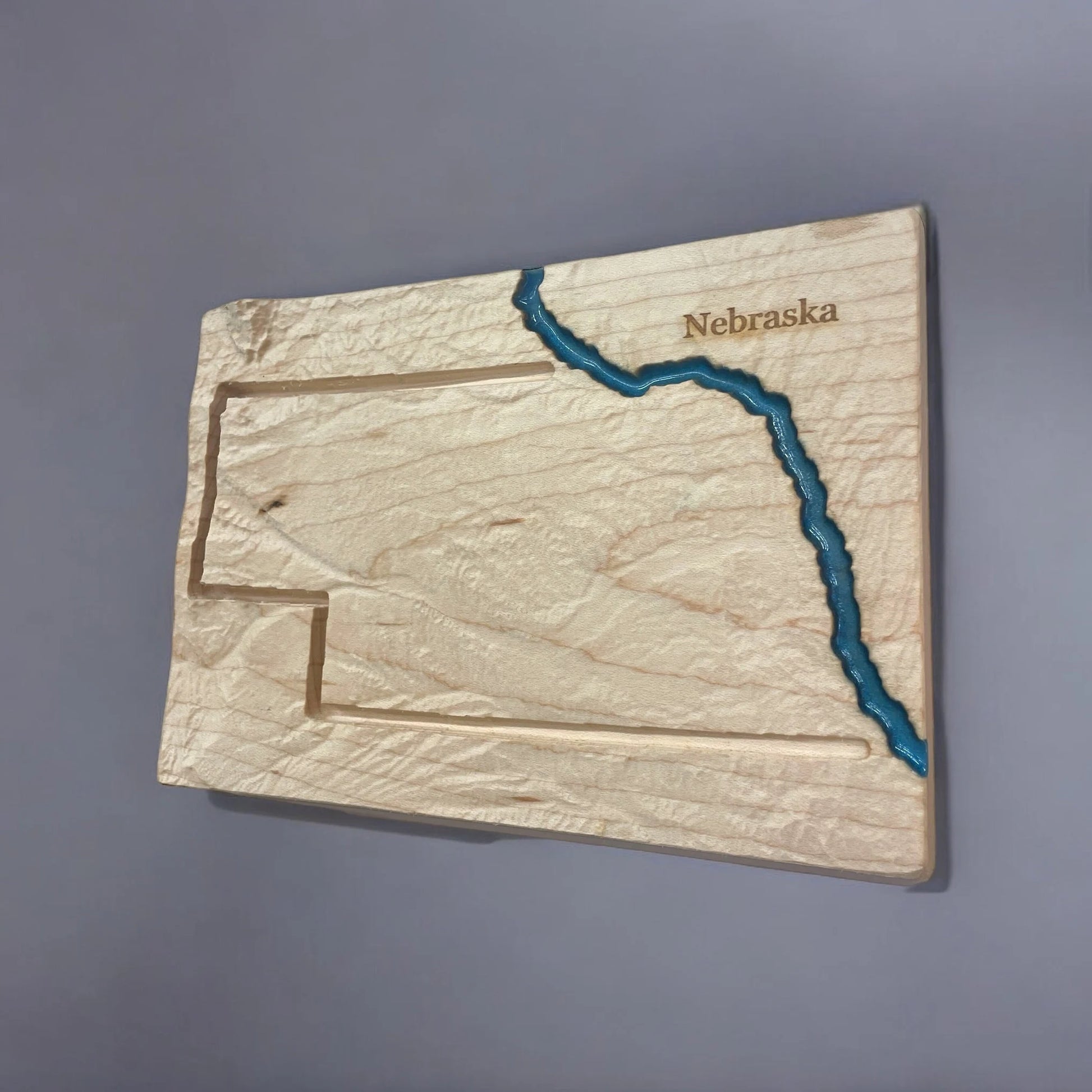 Wooden topo map of Nebraska with embossed topography and blue river, on a gray background