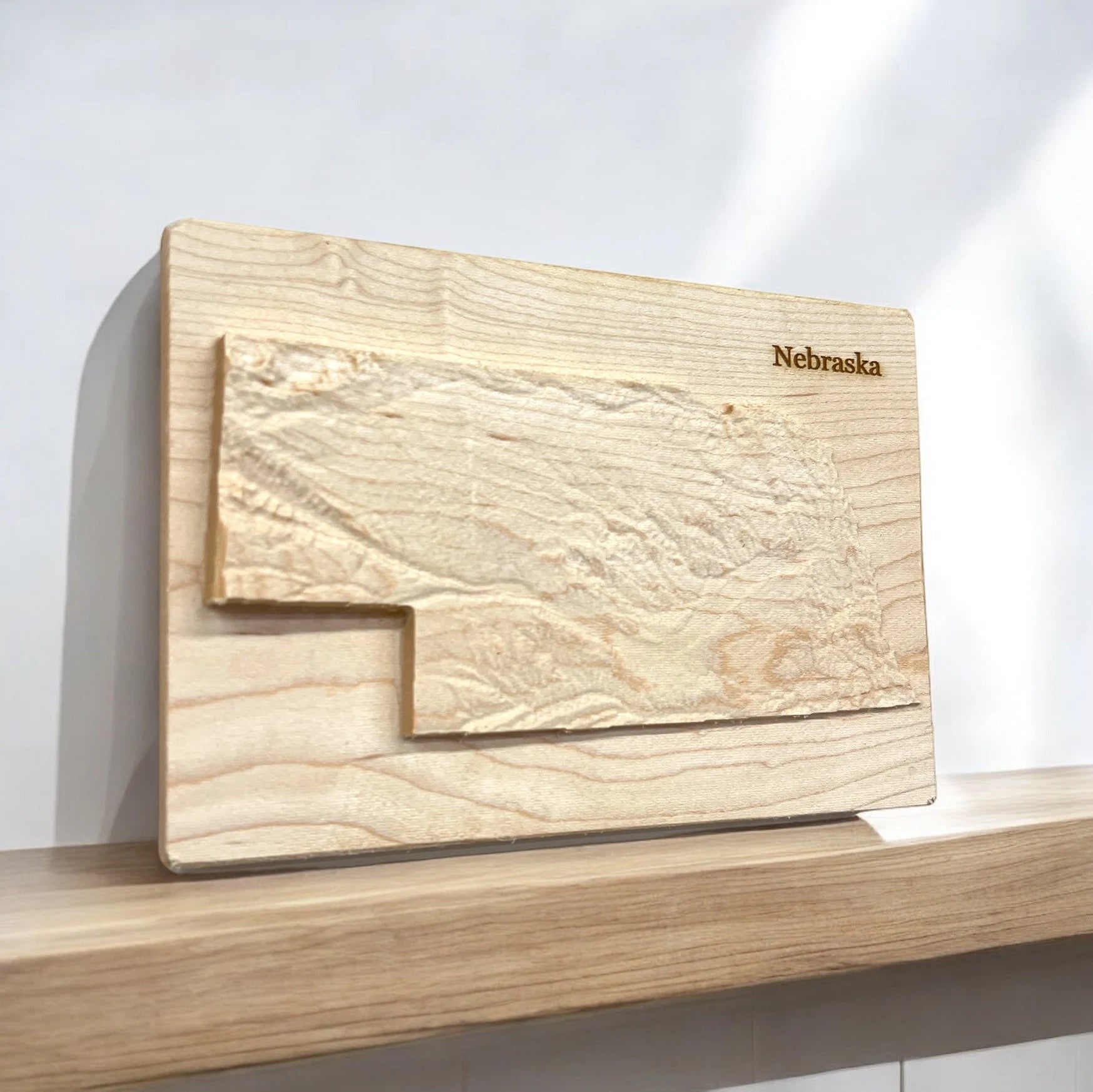 Wooden carved topo map of 'Nebraska' engraving on a light background