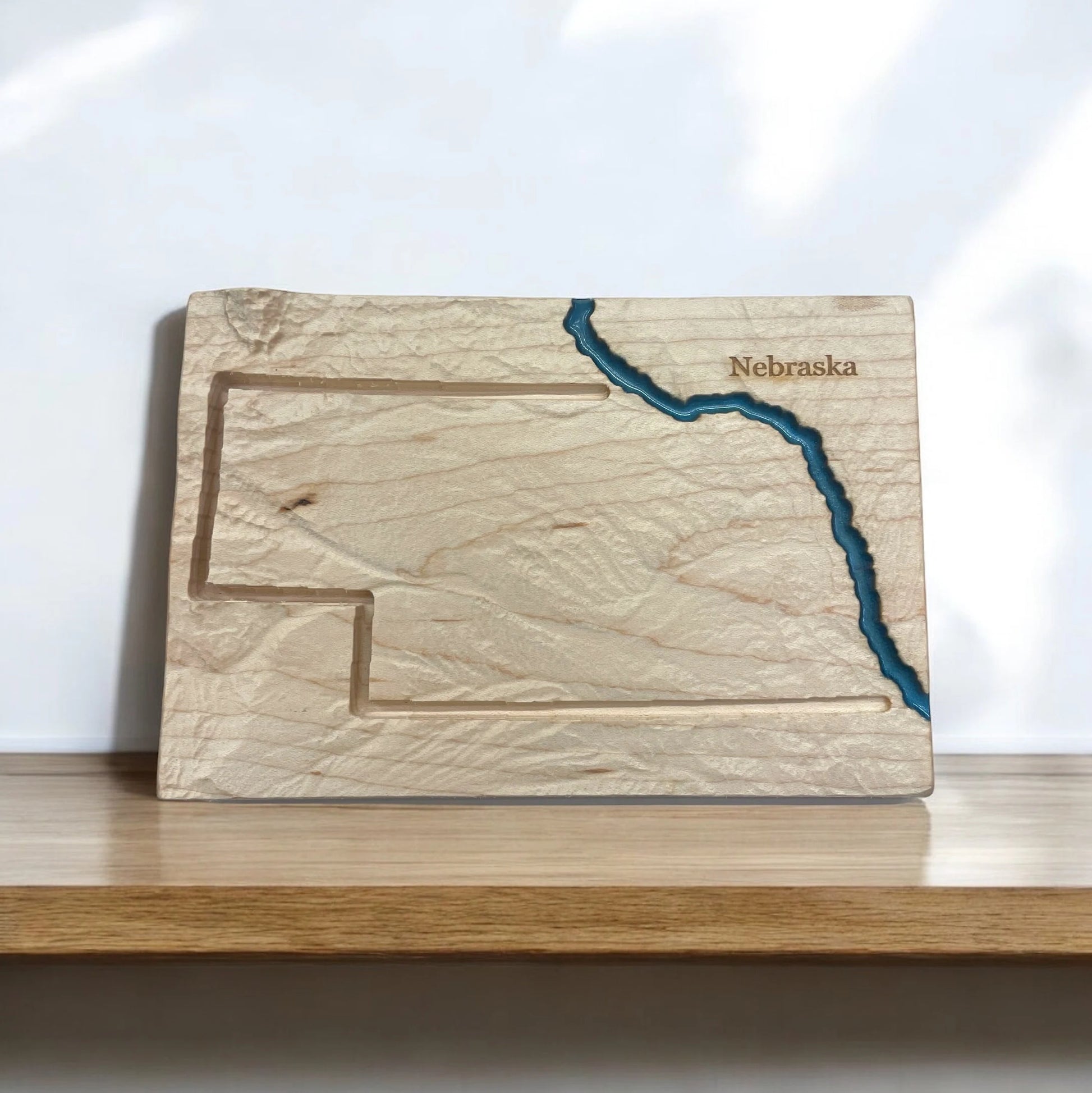 Wooden topo map with engraved outline of Nebraska on a white background