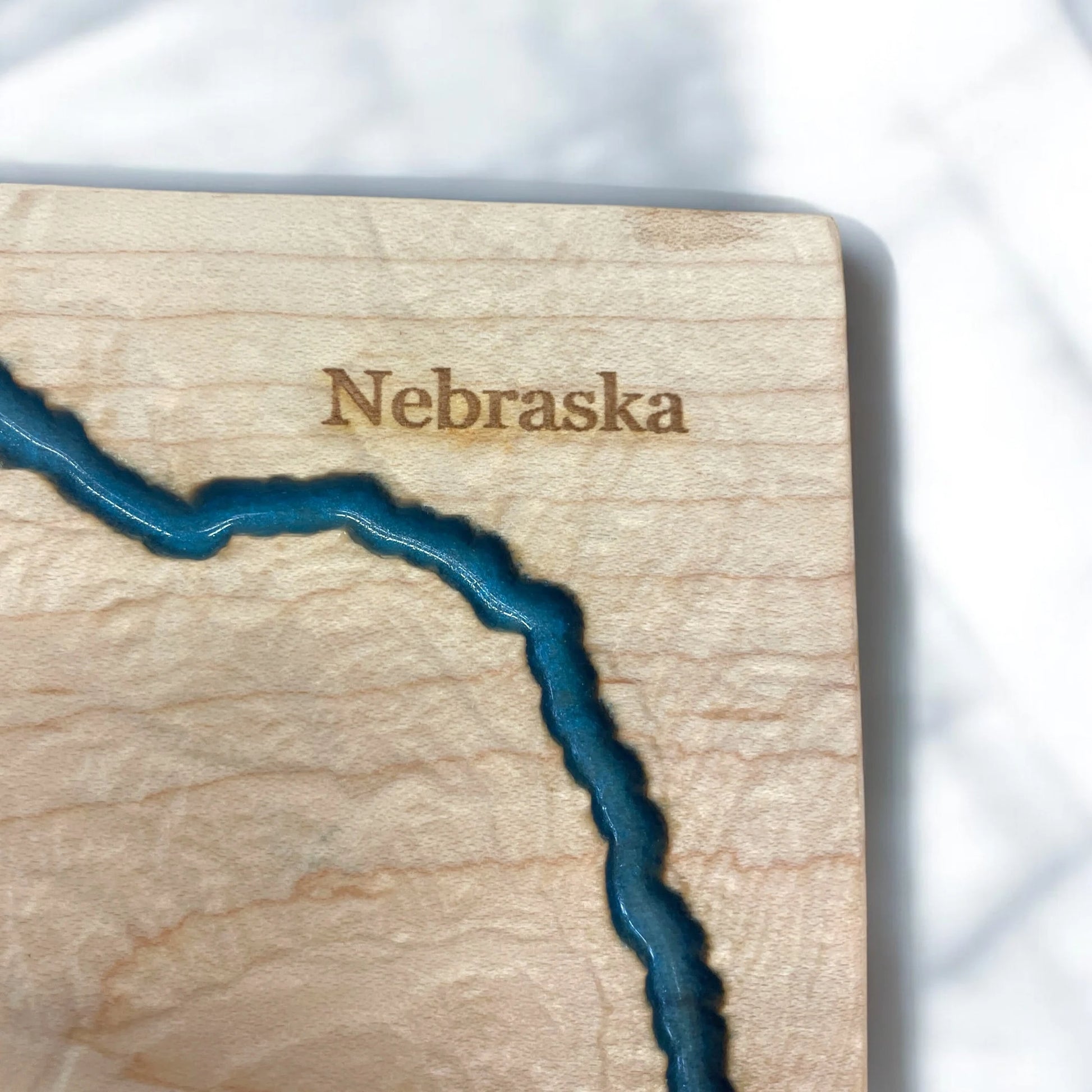 Wooden cutout of the state of Nebraska with blue water detail on a white background