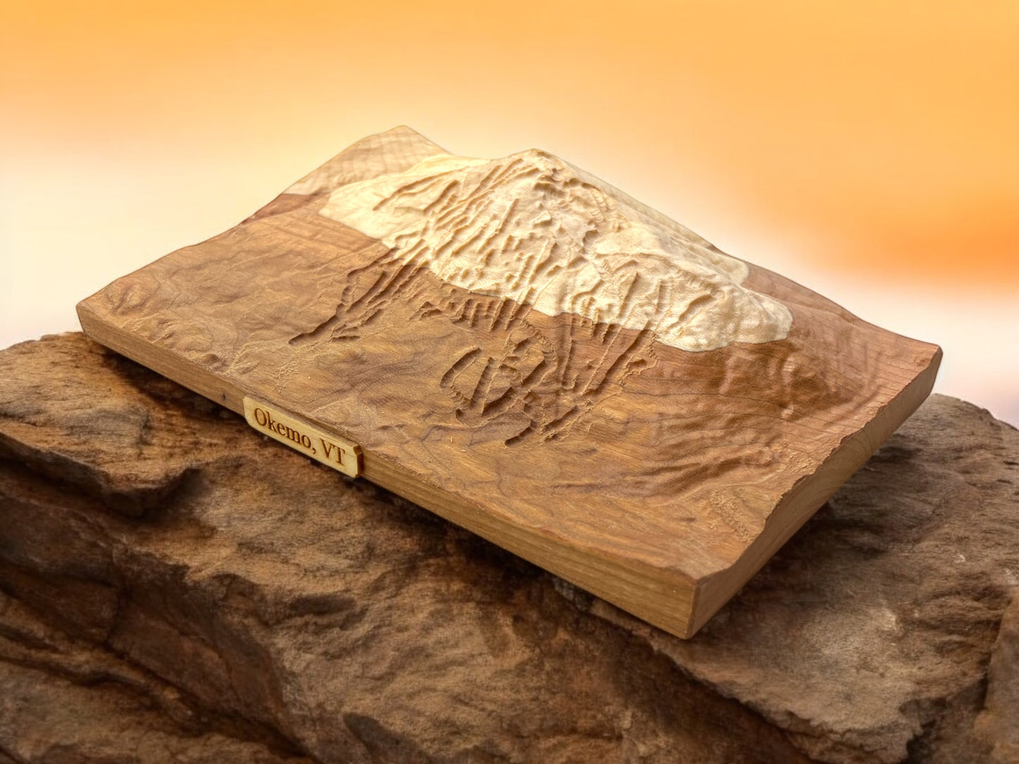 A wooden 3D relief ski map of Okemo Mountain, featuring topographic details, placed on a naturalistic surface.