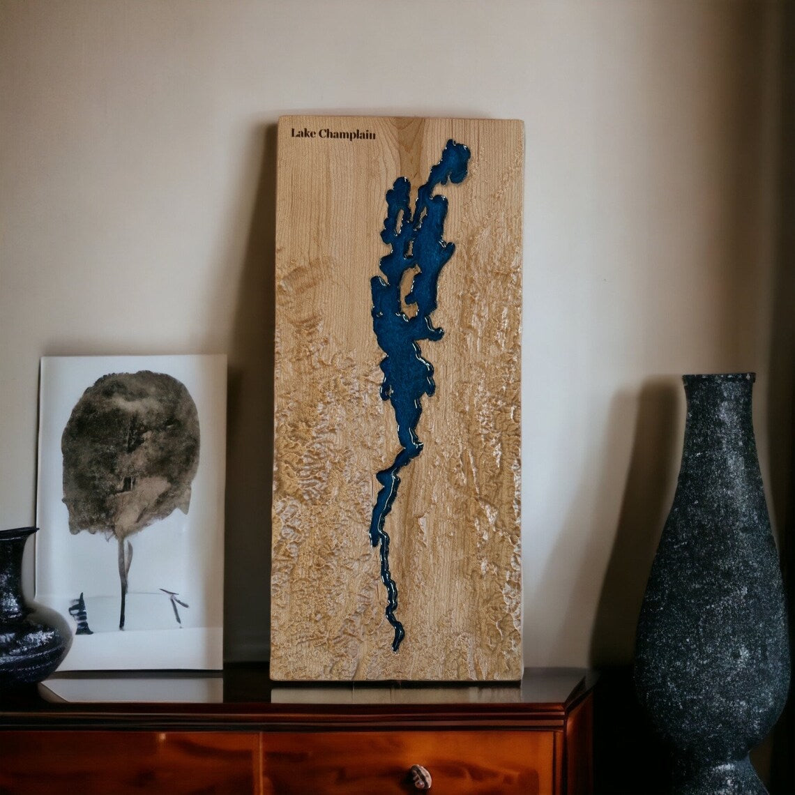Wooden map of Lake Champlain with blue outline on a shelf with decorative items.