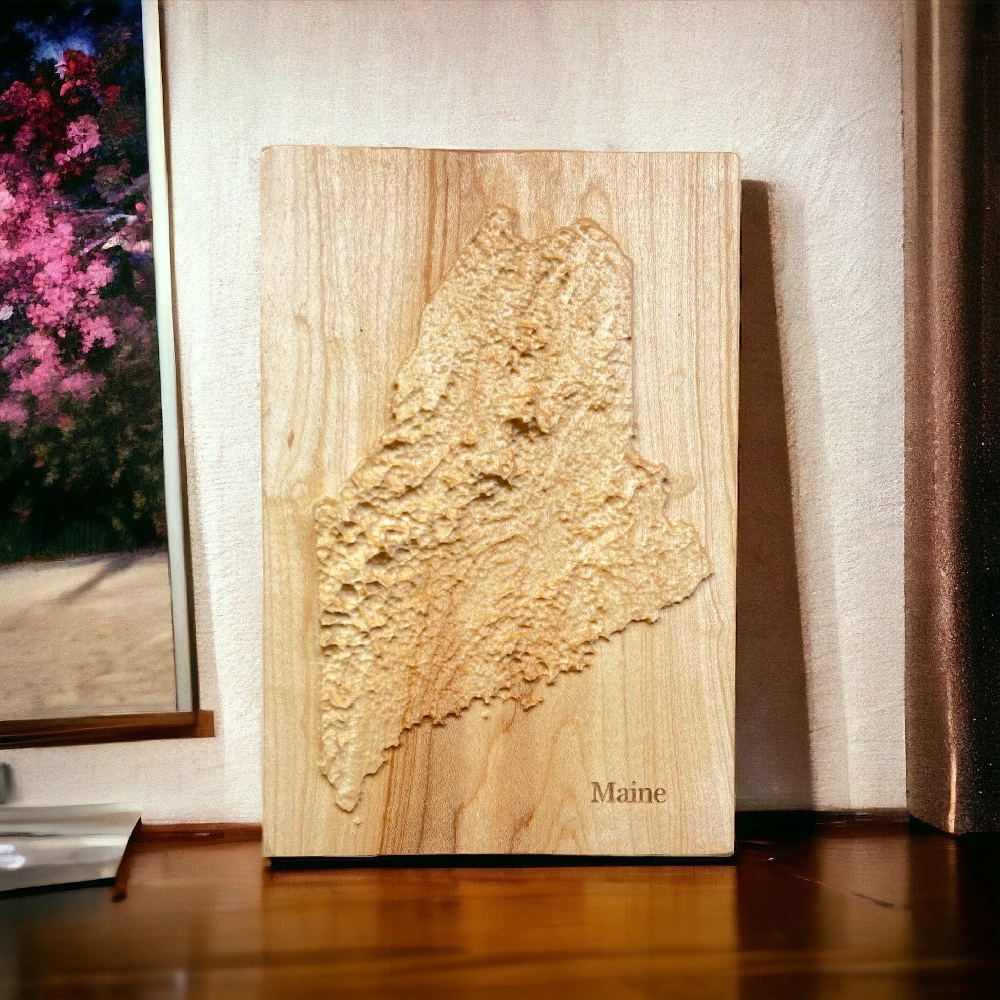 Wooden relief map of Maine on a wooden surface with a blurred background