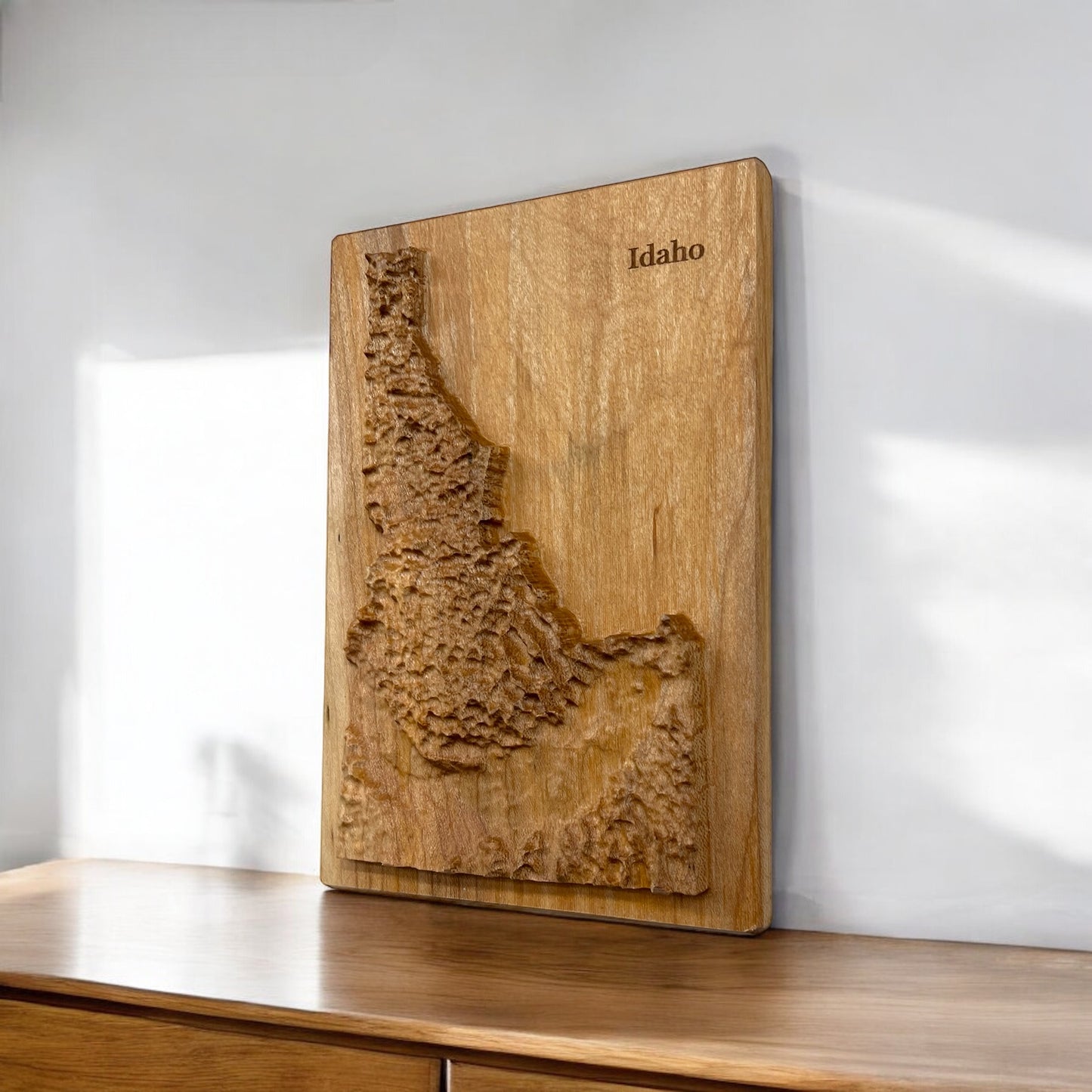 A wooden 3D relief map of Idaho on a wooden shelf against a white wall