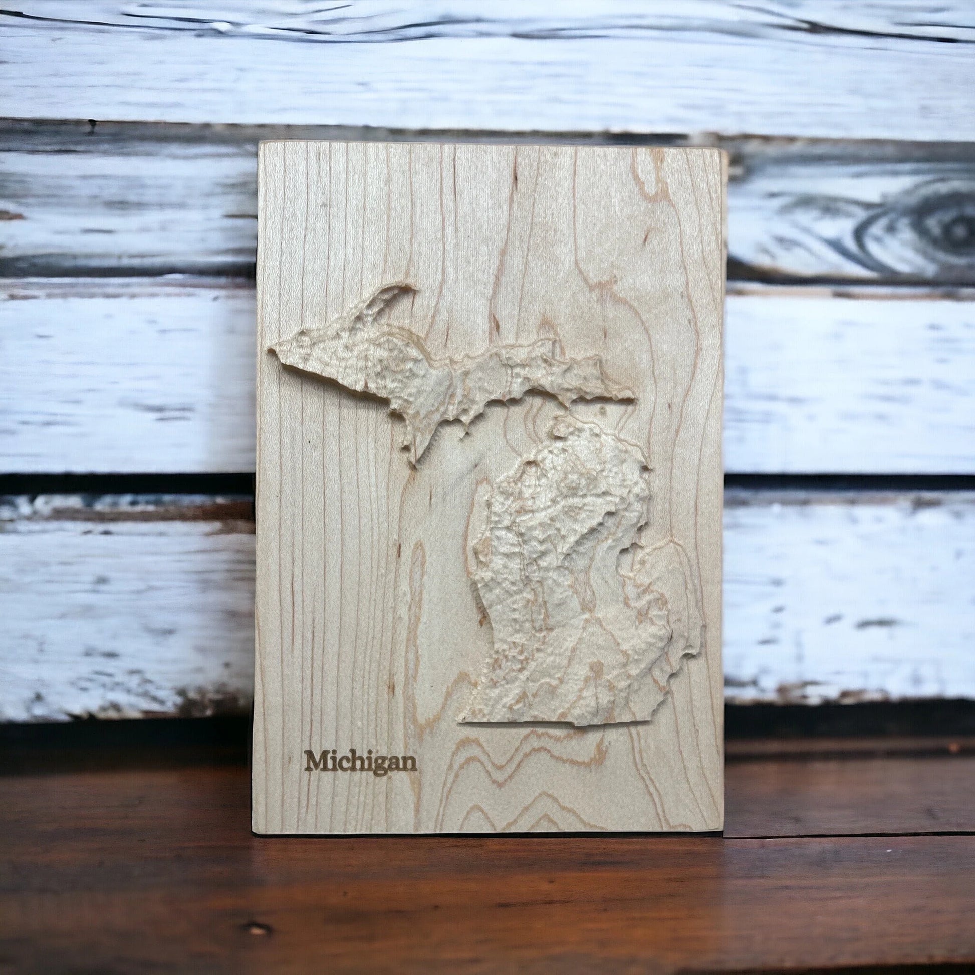 Wooden plaque with a topographic map of Michigan on a wooden surface.