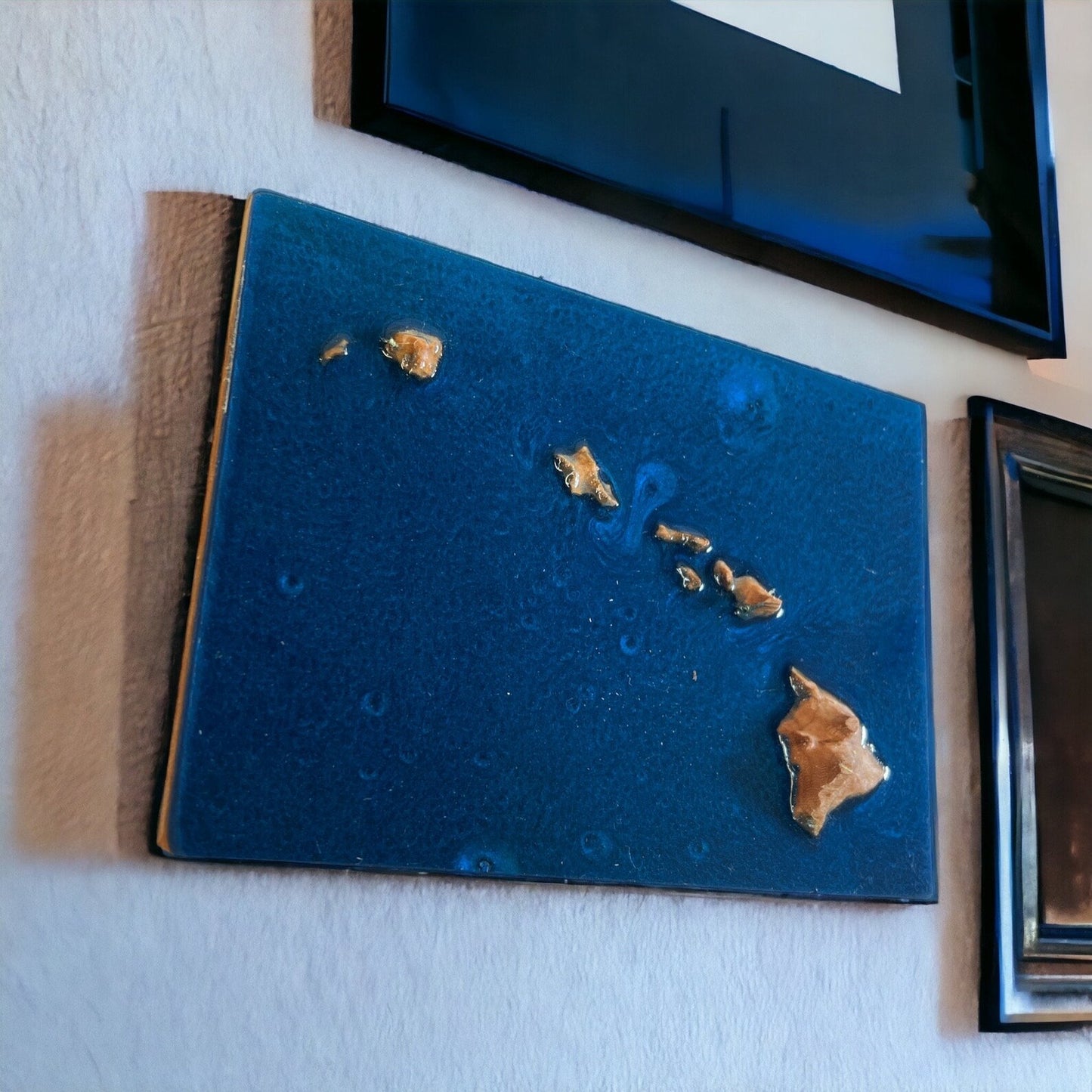 A wooden 3D topographic map of Hawaii with water featured in blue epoxy mounted on a wall, featuring relief to represent water bodies and landforms.