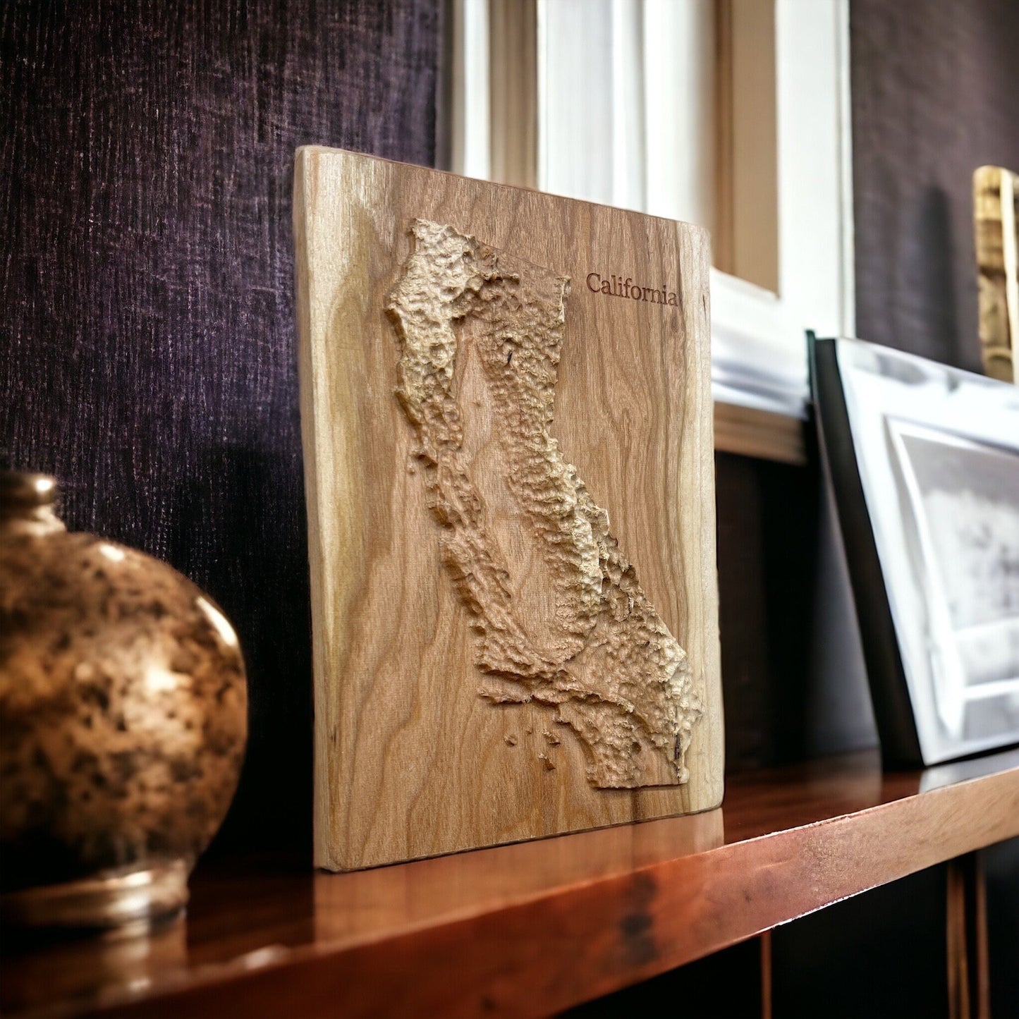 Wooden relief map of California on a shelf with decorative items.
