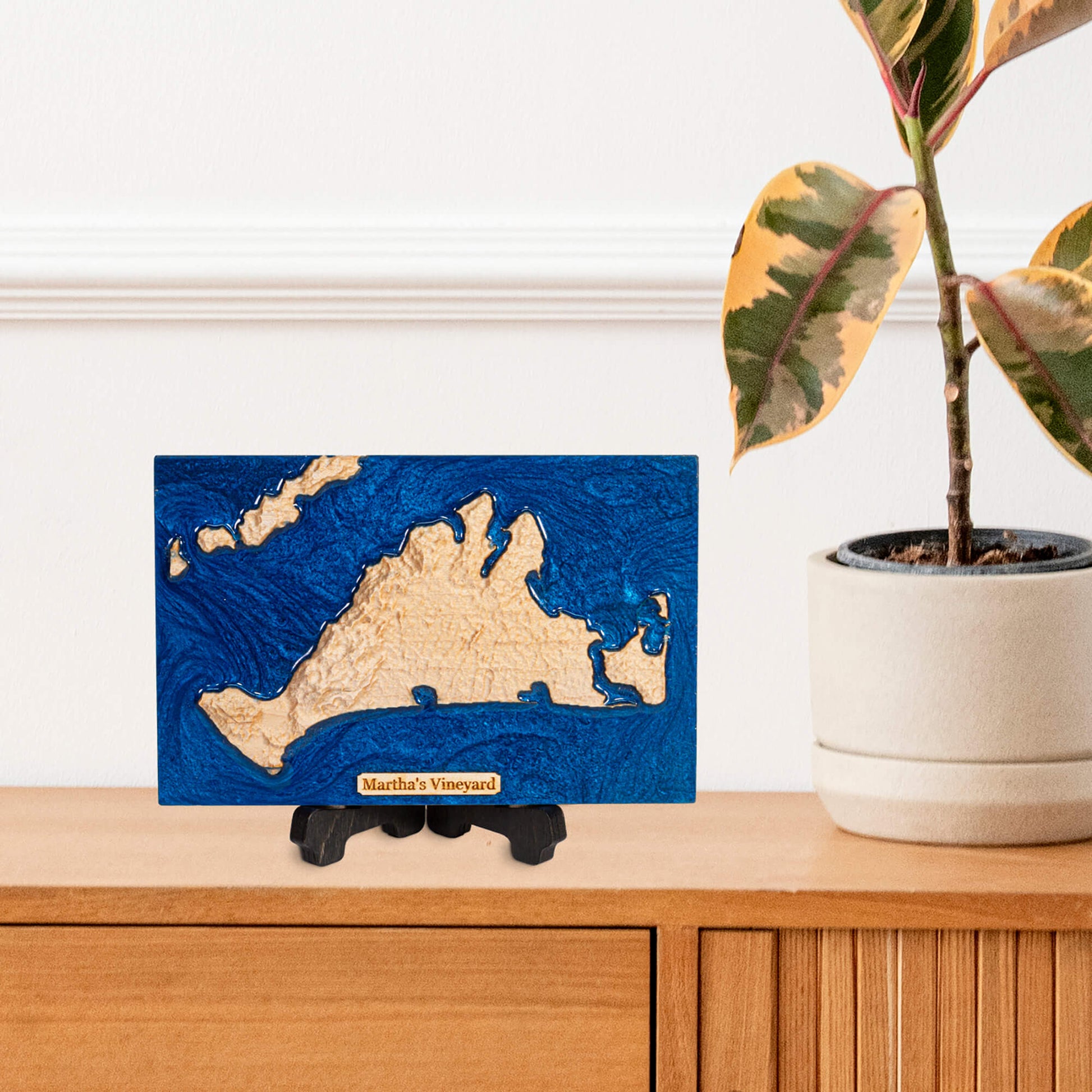 wooden carved map of marthas vinyard on a display stand on a wooden cabinet with a plant