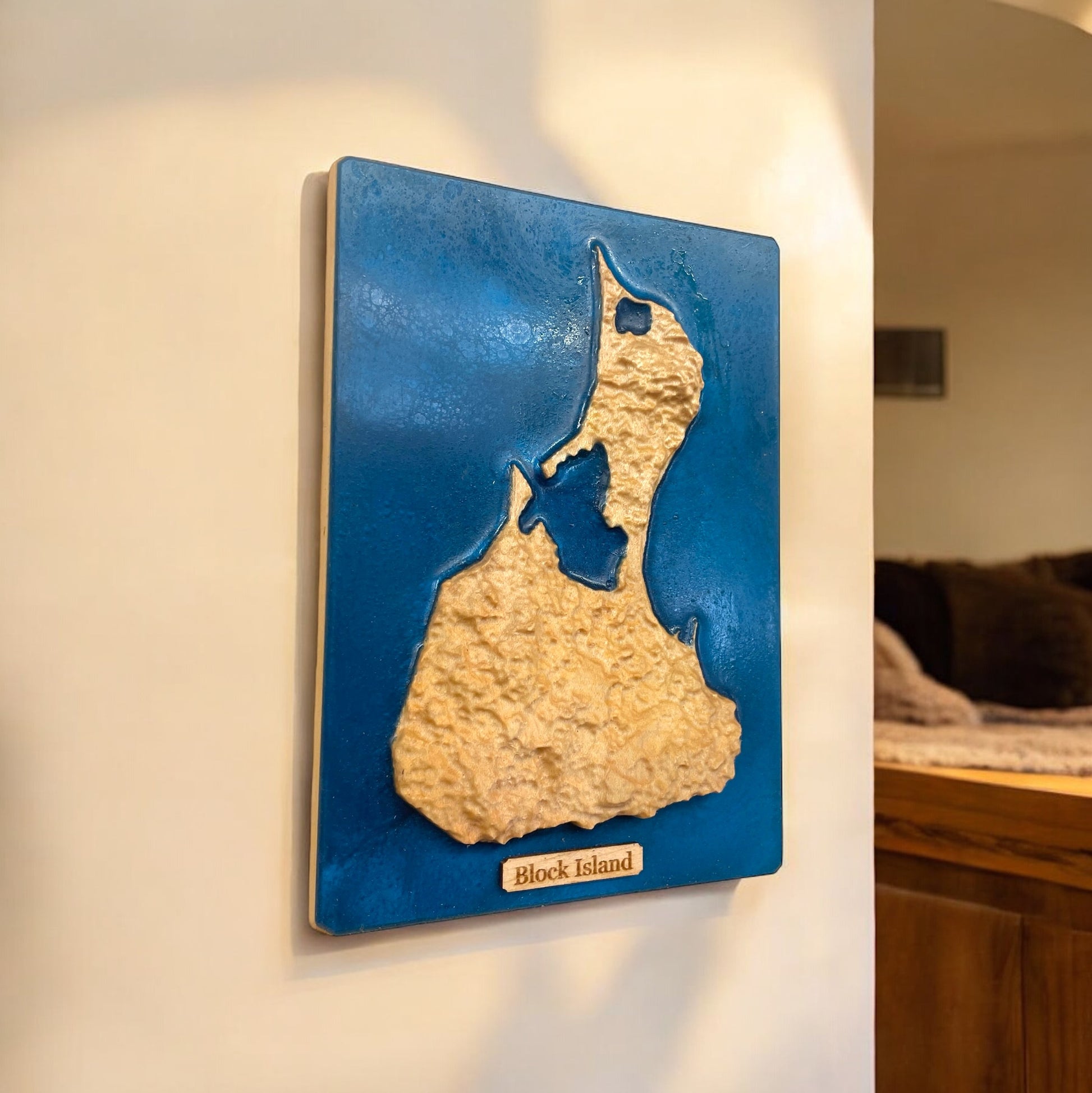A 3D relief map of Block Island, Rhode Island, mounted on a wall, with blue epoxy resin representing water and a wooden relief of the land shape.