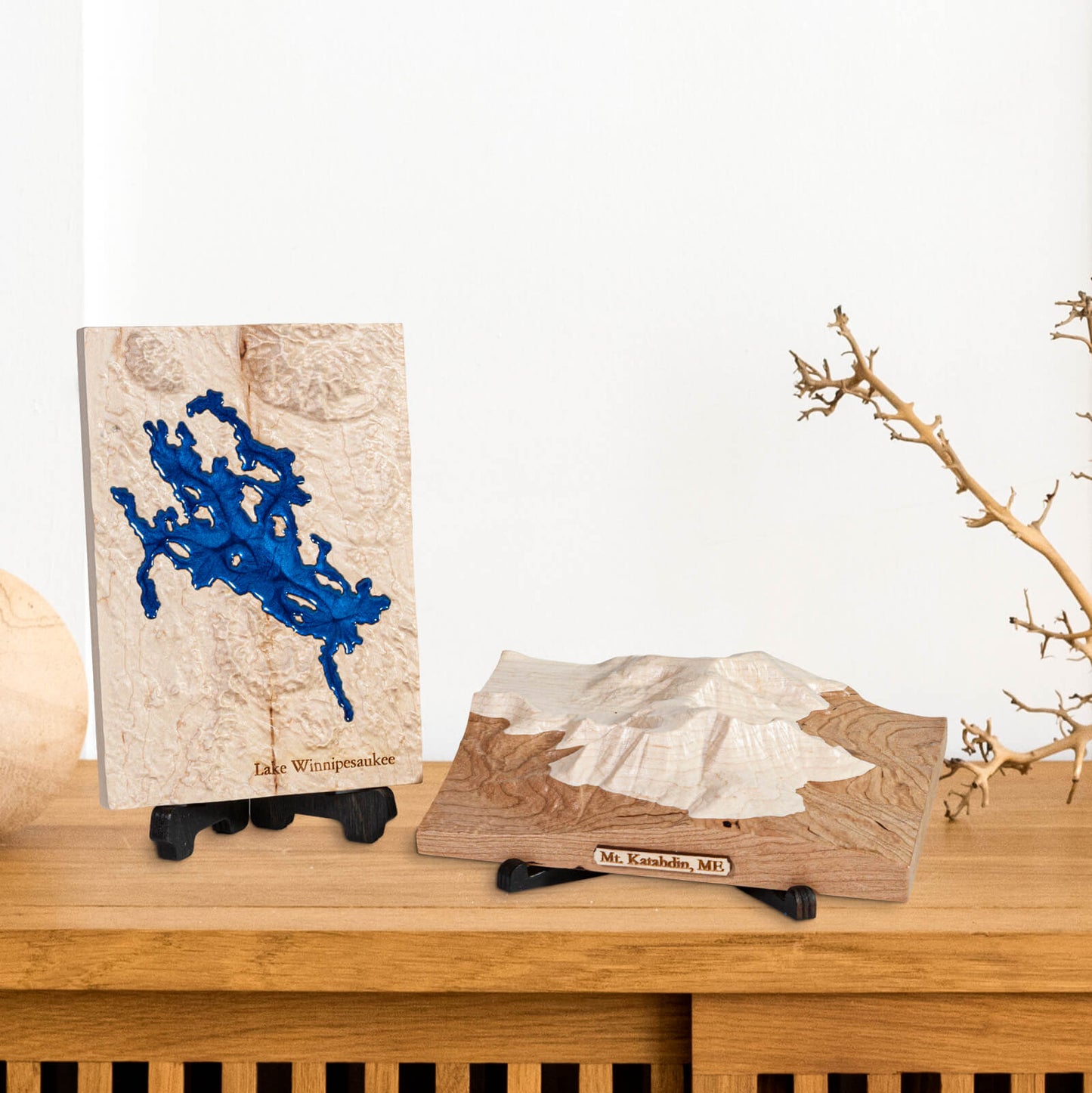 two carved wooden maps, one of Lake Winnipesaukee and Mt. Katahdin placed on stands, on a shelf in a home.