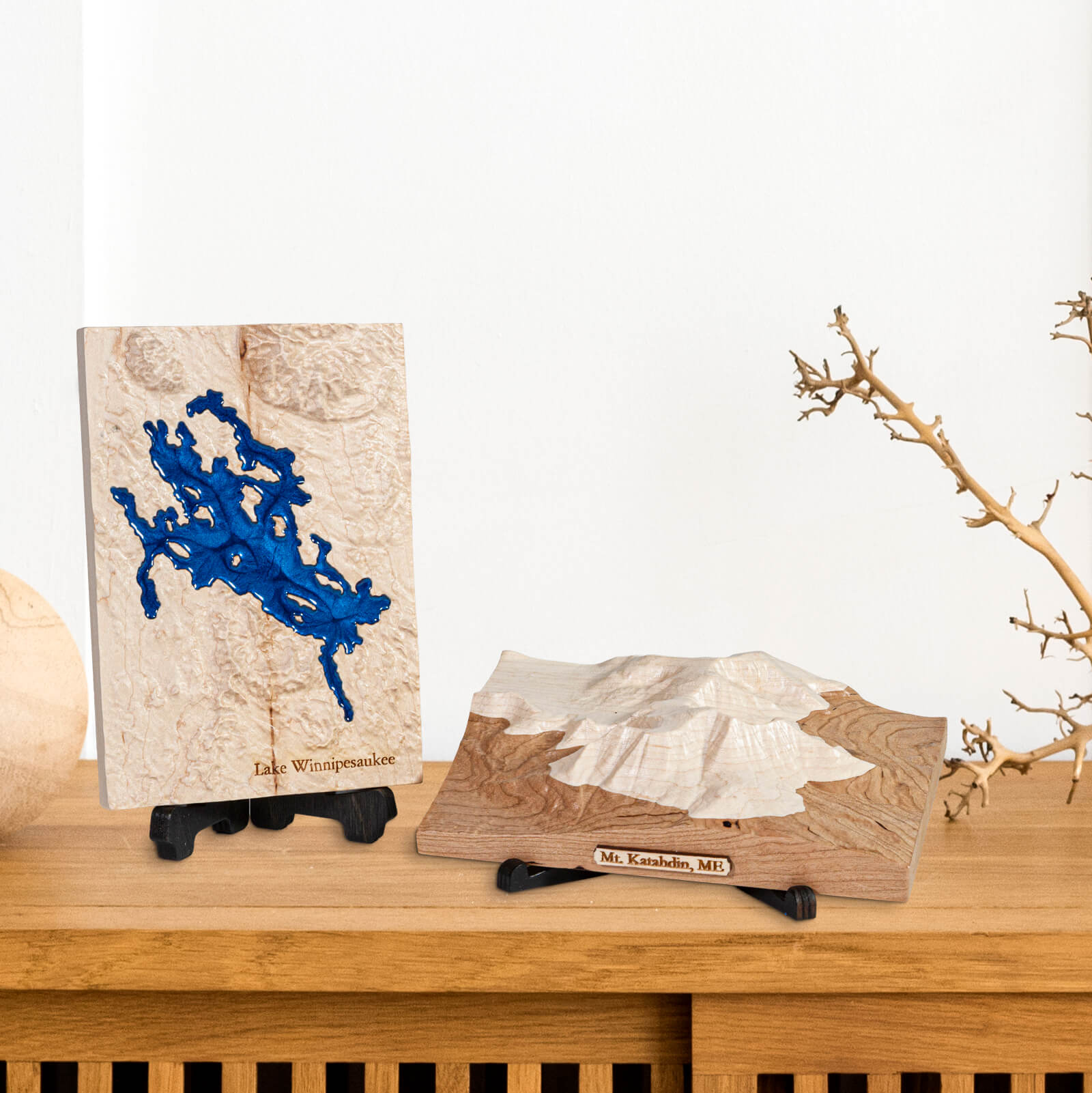 two carved wooden maps, one of Lake Winnipesaukee and Mt. Katahdin placed on stands, on a shelf in a home.