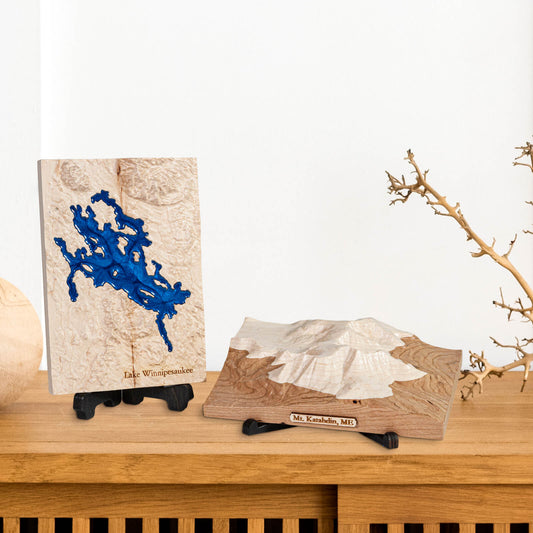 two carved wooden maps, one of Lake Winnipesaukee and Mt. Katahdin placed on stands, on a shelf in a home.