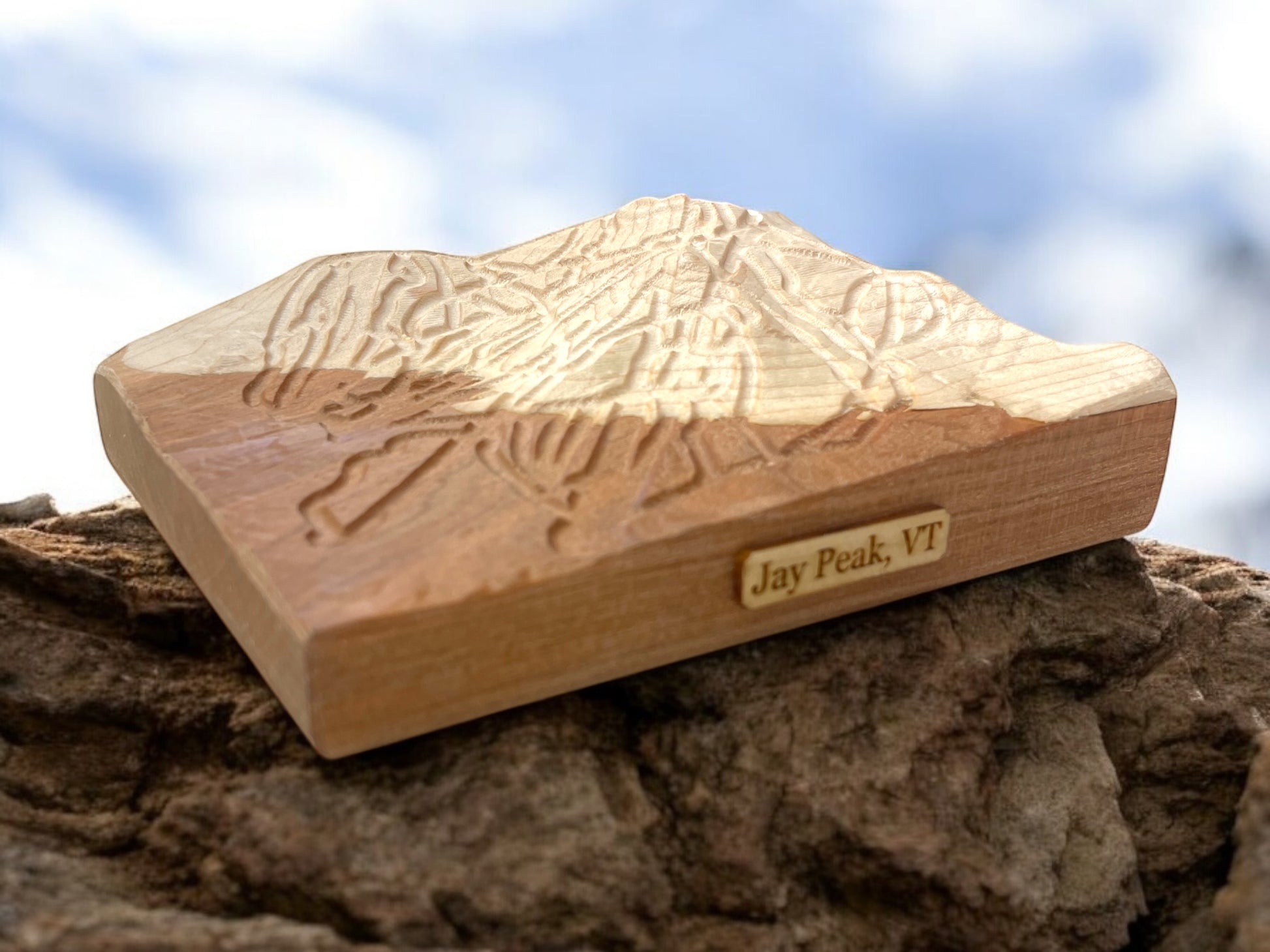 A wooden 3D relief ski map of Jay Peak Ski Mountain, Vermont, with intricate carvings, placed on a natural rock surface.