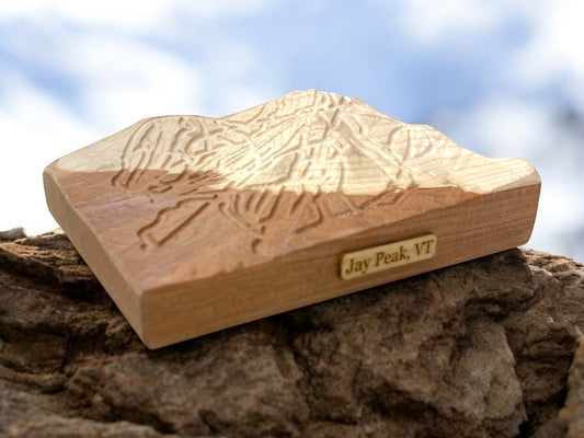 A wooden 3D relief ski map of Jay Peak Ski Mountain, Vermont, with intricate carvings, placed on a natural rock surface.
