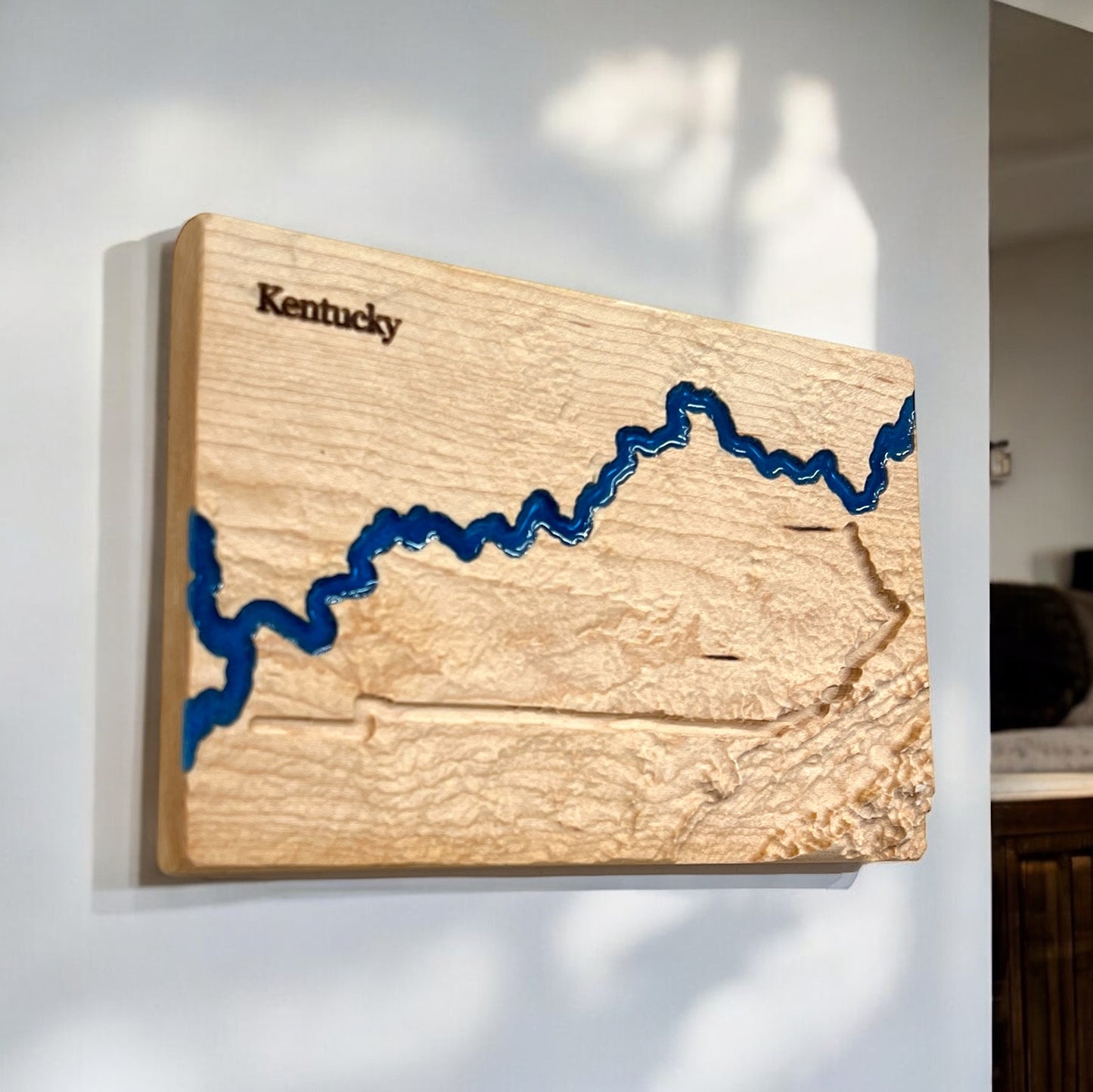 A wooden 3D relief map of Kentucky with blue epoxy resin depicting water features.