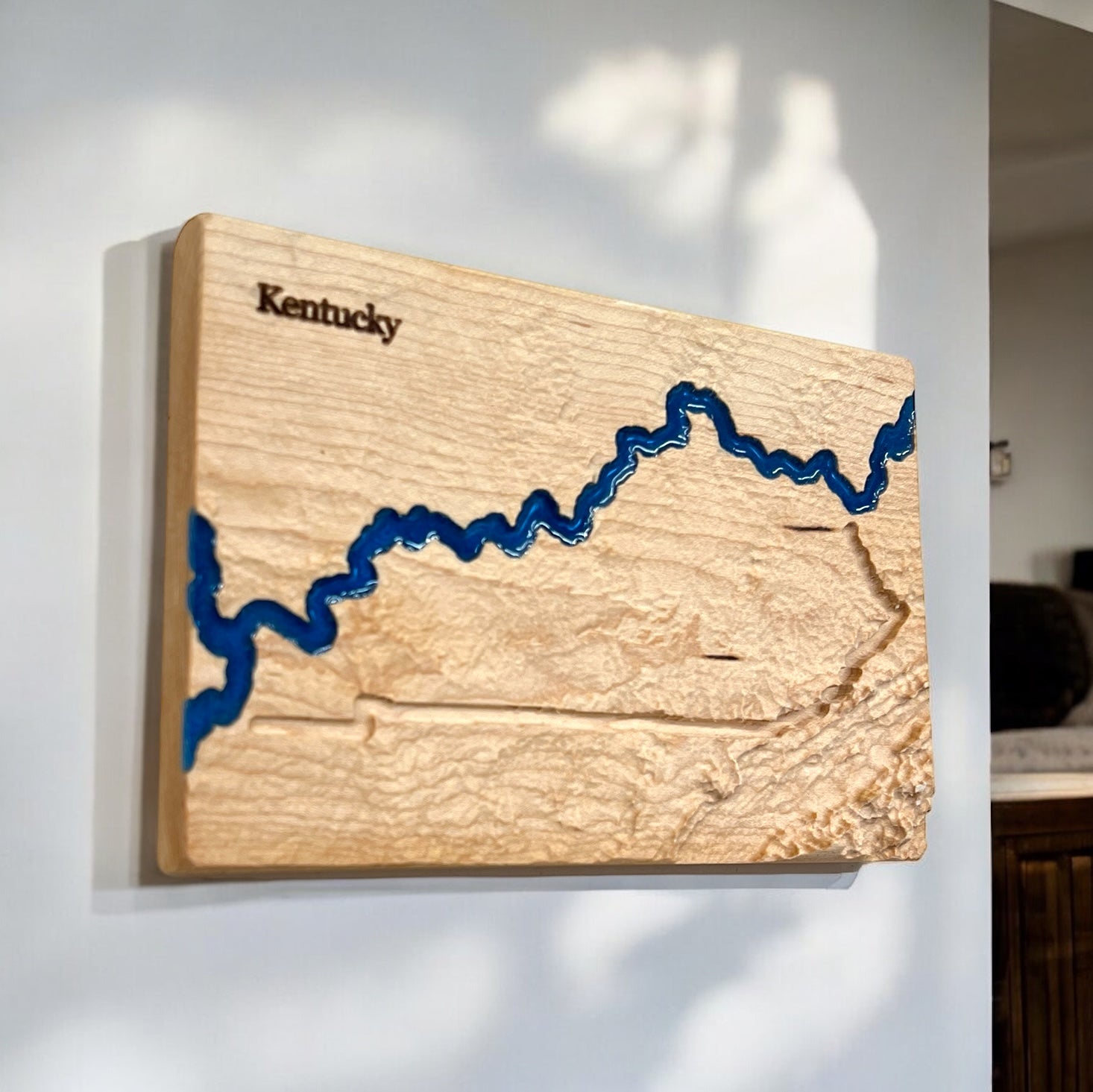 A wooden 3D relief map of Kentucky with blue epoxy resin depicting water features.