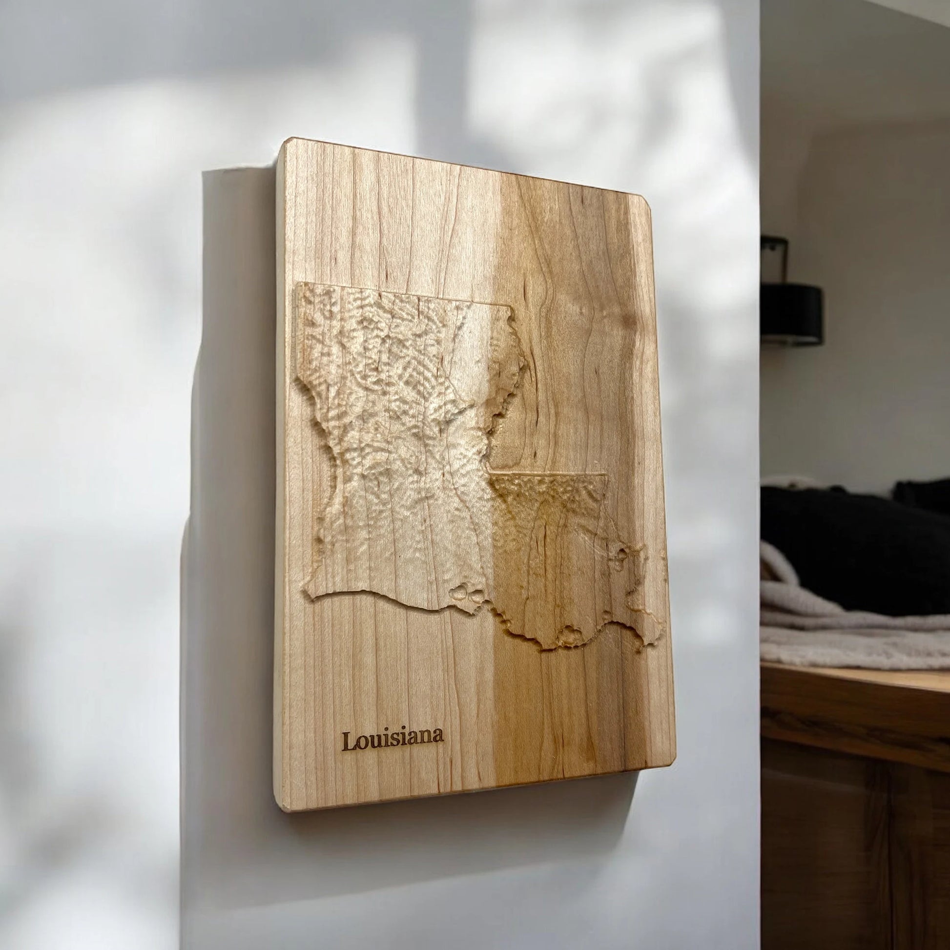 Wooden wall art with a topographic map of Louisiana on a white wall.