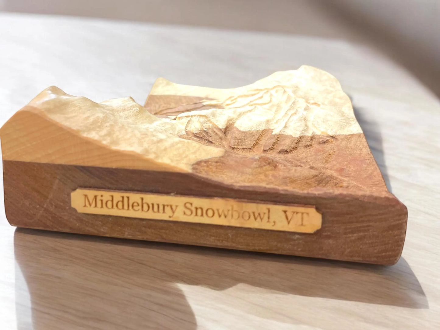 Wooden carving of Middlebury Snow Bowl  with 'Middlebury Snowbowl, VT' plaque engraving on a reflective surface