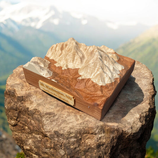 A wooden 3D relief map of Mt Washington, placed on a rock with a scenic landscape in the background.