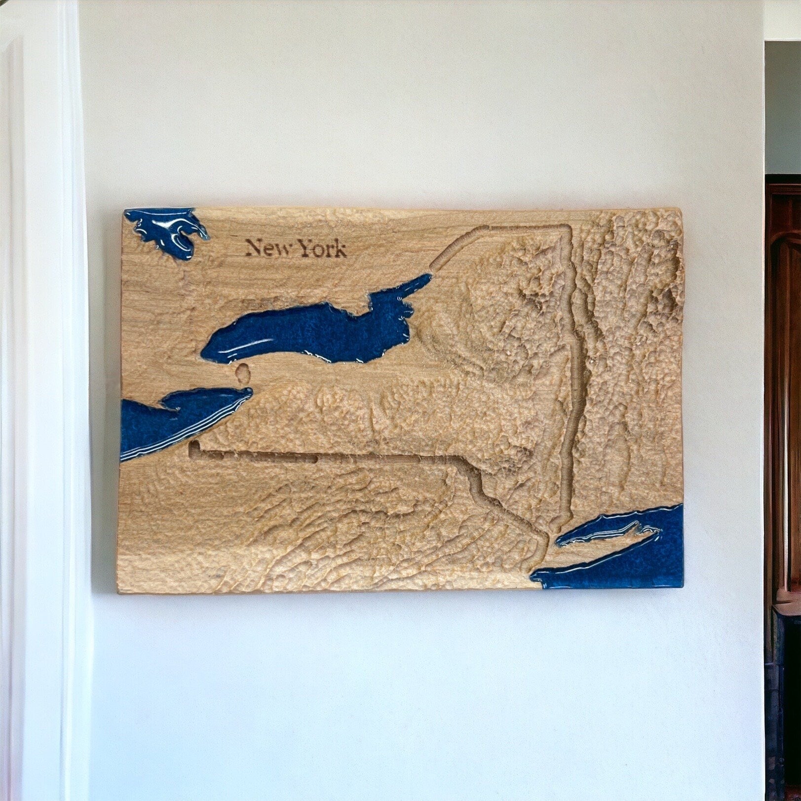Wooden relief map of New York with great lakes and ocean water features in blue on a white wall