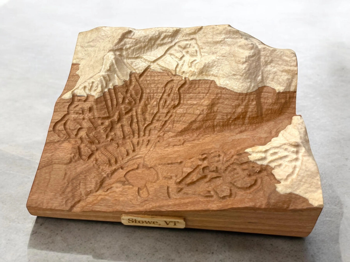 Wooden topographic model of a landscape with 'Stowe, VT' on a white background