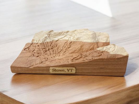 A wooden 3D relief ski map of Stowe, VT, featuring detailed topography, placed on a wooden surface.