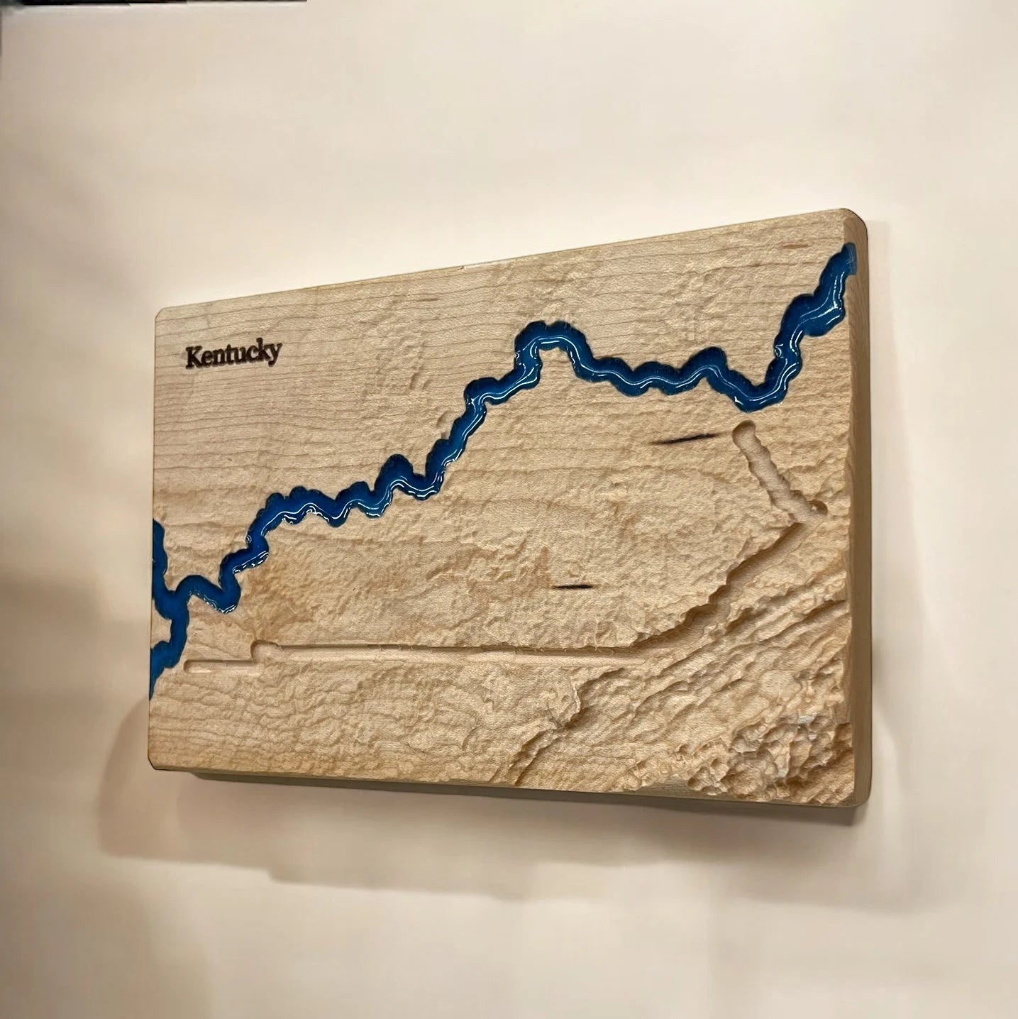 Wooden wall art of Kentucky with a blue river outline on a beige background