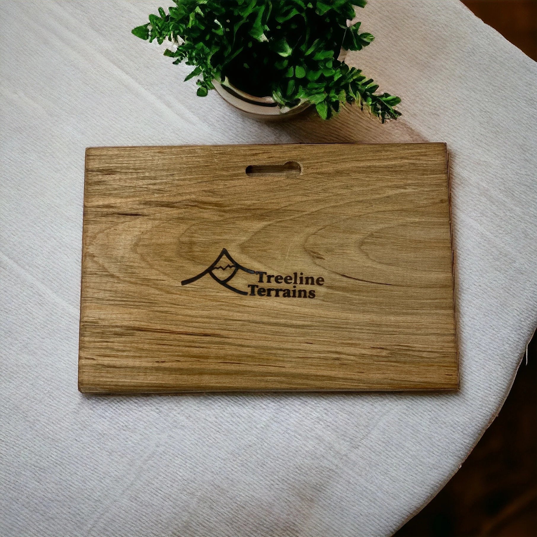 Wooden plaque backside detail of keyhole with 'Treeline Terrains' logo on a white surface with a plant in the background