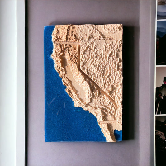 A 3D relief map of California made of wood and blue epoxy resin, mounted on a wall.