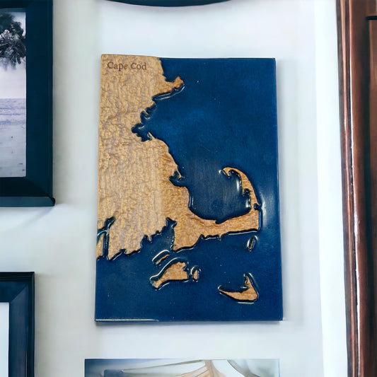 A 3D topographic wood map of Cape Cod, with relief depicting the landscape. The map is primarily in shades of blue and beige, with the ocean in blue and the land in beige.