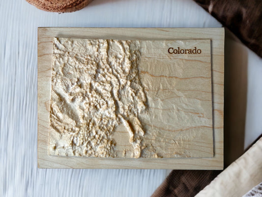 A wooden map of Colorado with relief detailing, made from locally-sourced wood on a table top