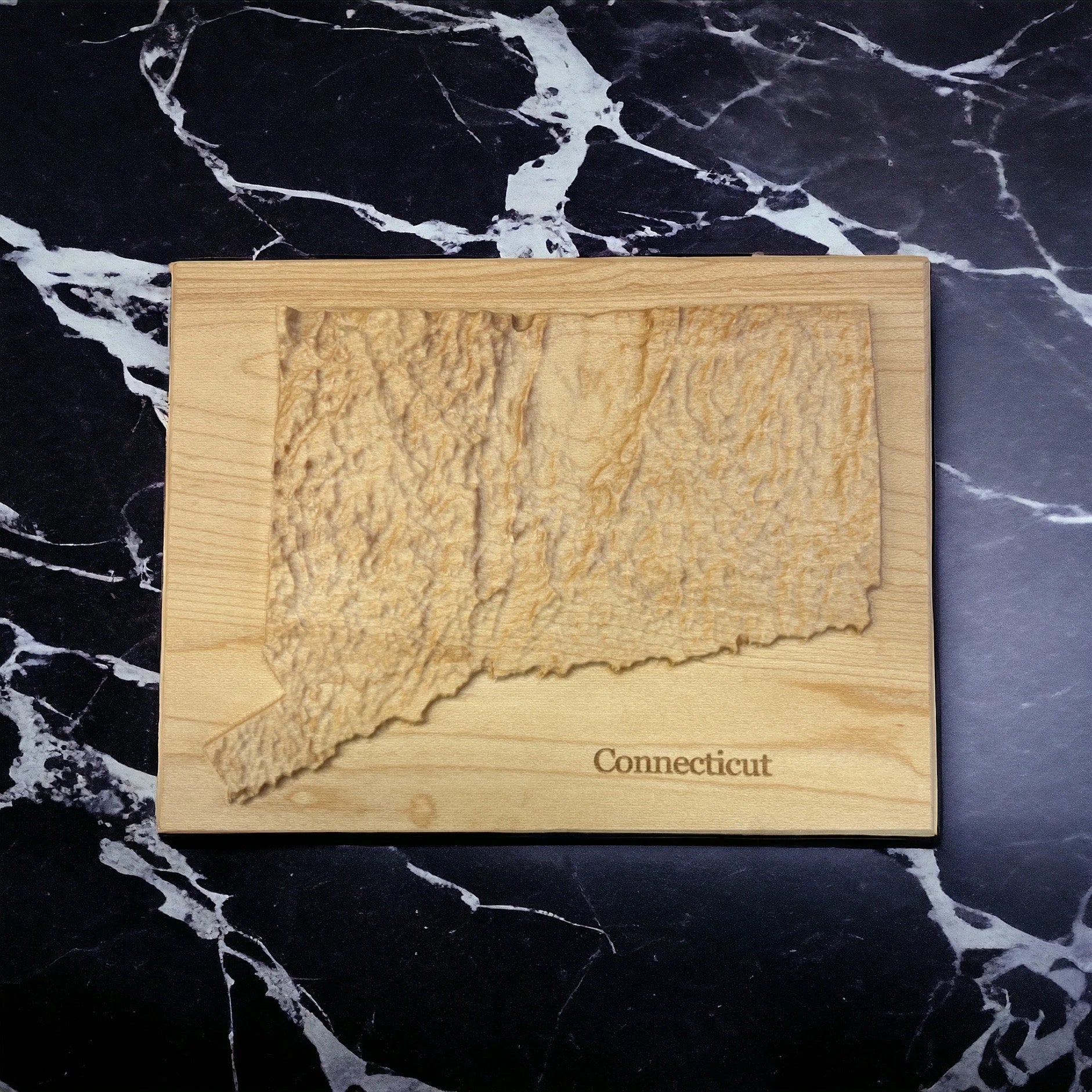 Wooden cutting board with a raised map of Connecticut on a black marble surface