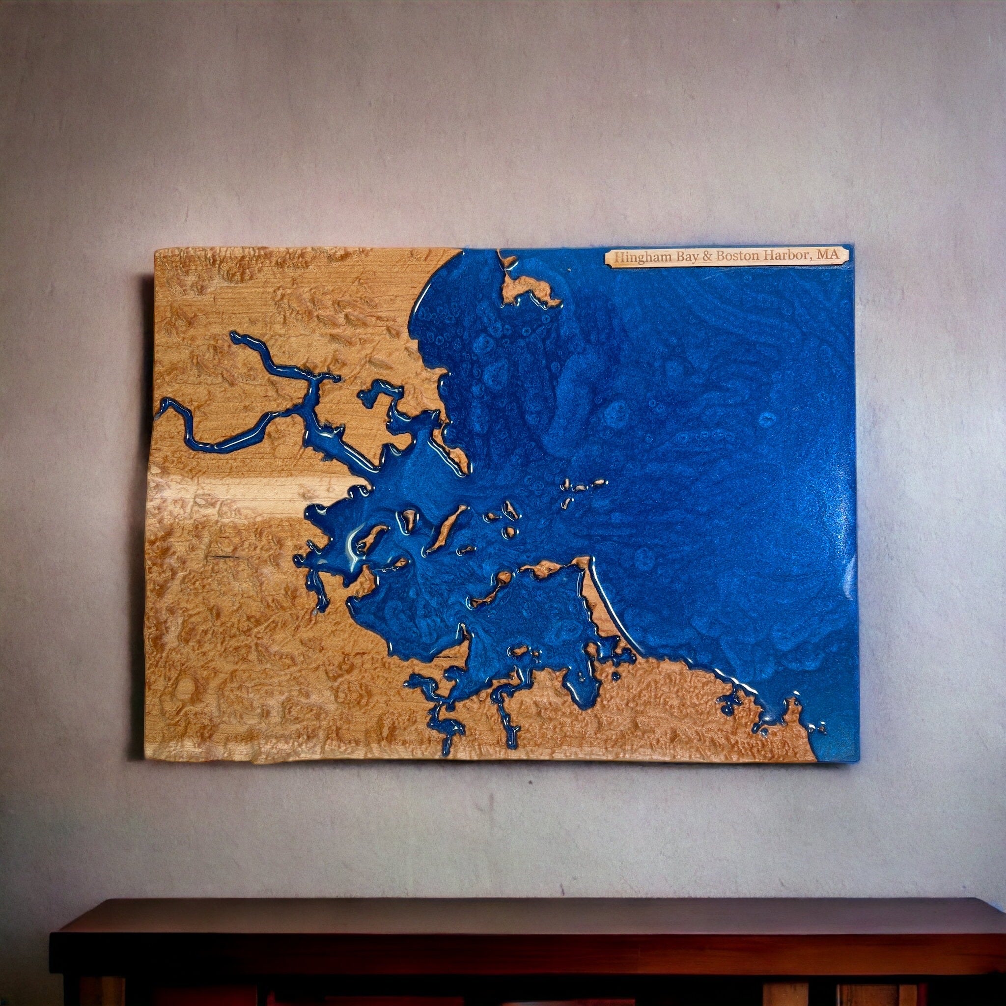 a topographic wooden map with epoxt for water of hingham bay and boston harbor hanging on a wall above wooden furniture