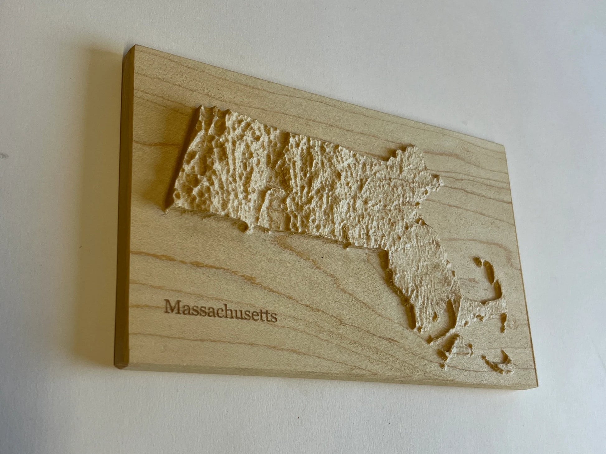 Wooden plaque with a textured map of Massachusetts on a white background