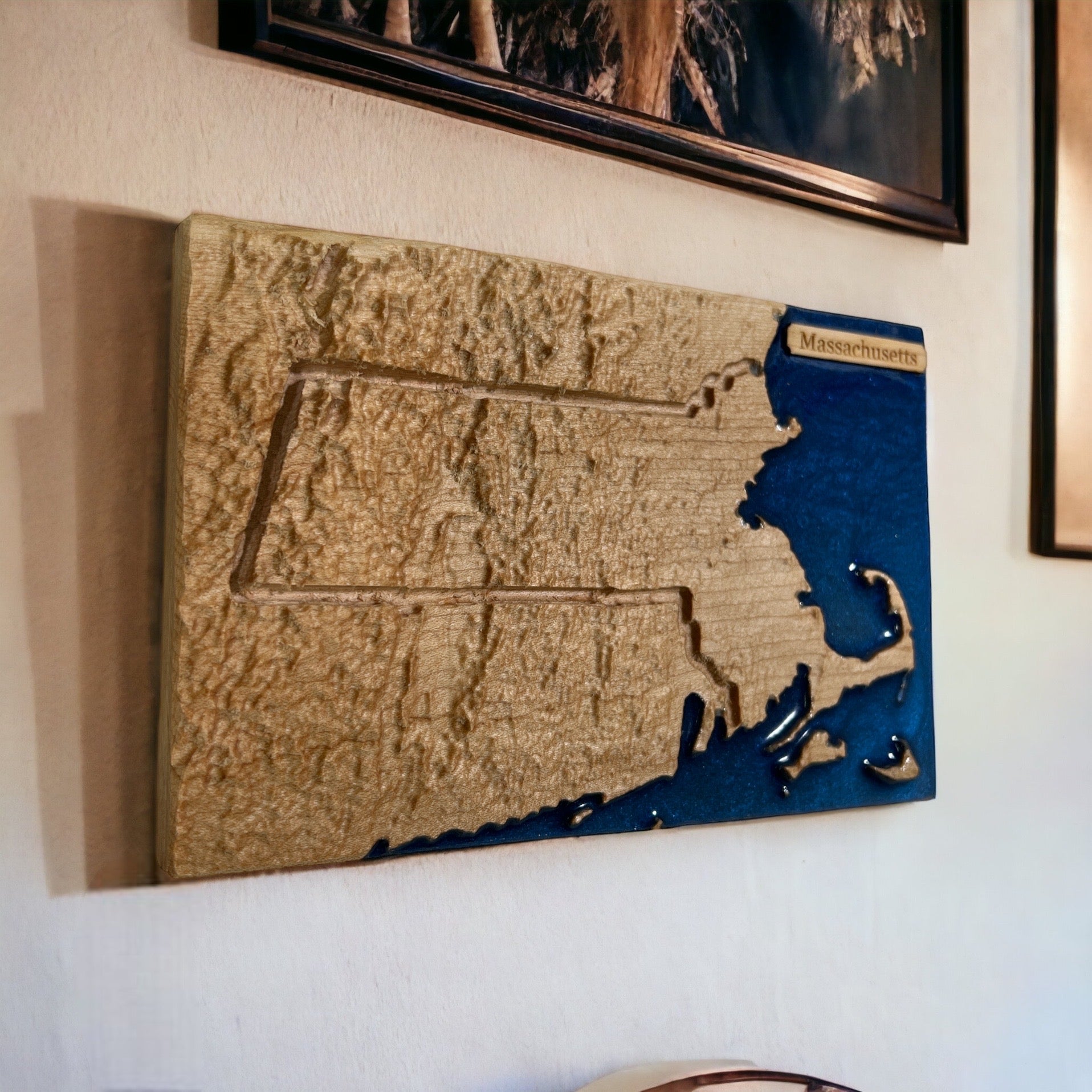 wooden topo 3d map of massachusetts hangin on a wall with other pictures on a white wall