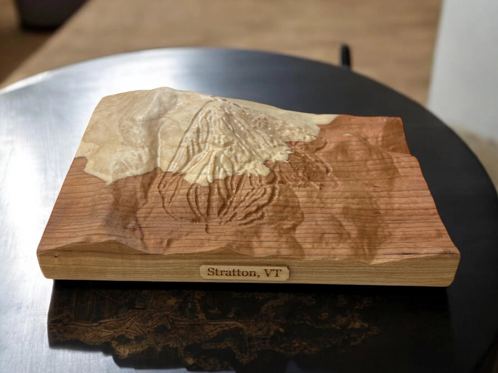 Wooden topographic model of Stratton Mountain ski resort with a 'Stratton, VT' plaque mounted on it, placed on a metallic surface.