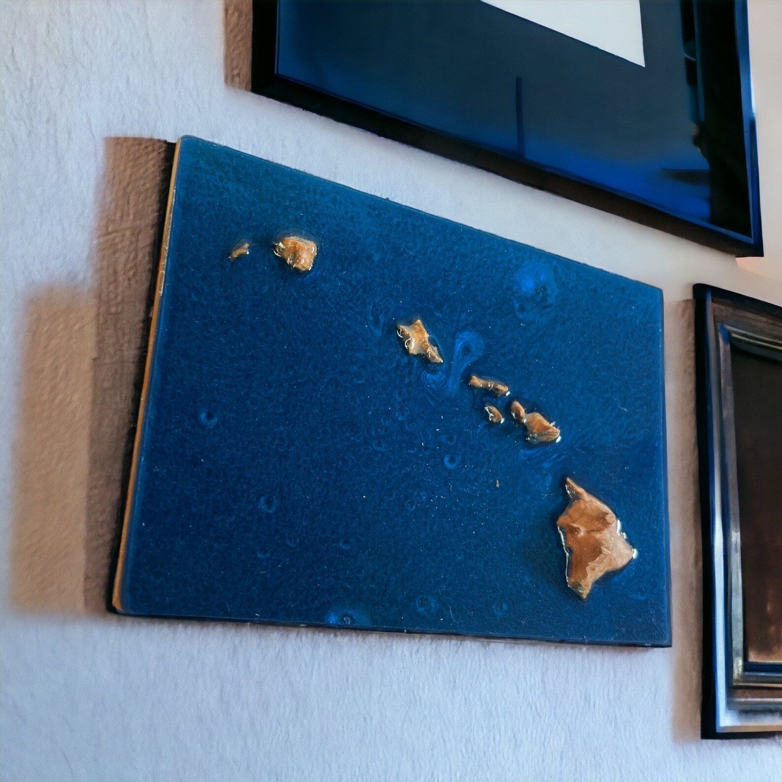 A wooden 3D topographic map of Hawaii with water featured in blue epoxy mounted on a wall, featuring relief to represent water bodies and landforms.