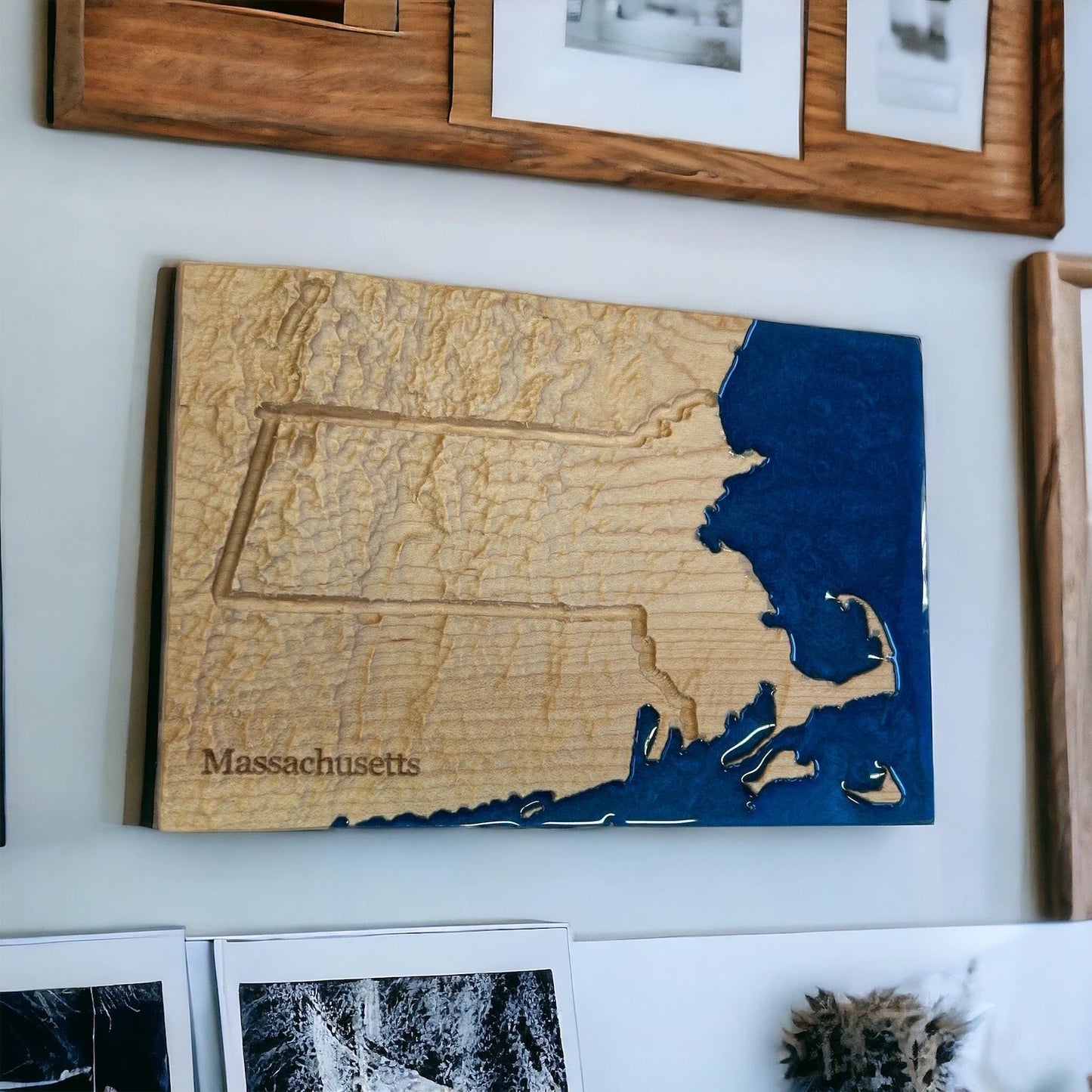 Wooden carved topographic map of Massachusetts on a wall with framed pictures above